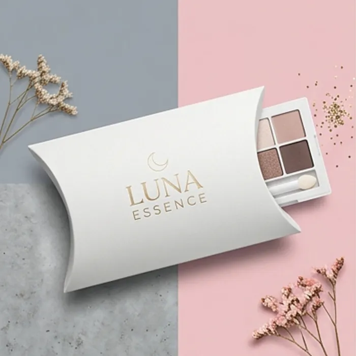 White cosmetic pillow box with a minimal wordmark beside an eyeshadow palette