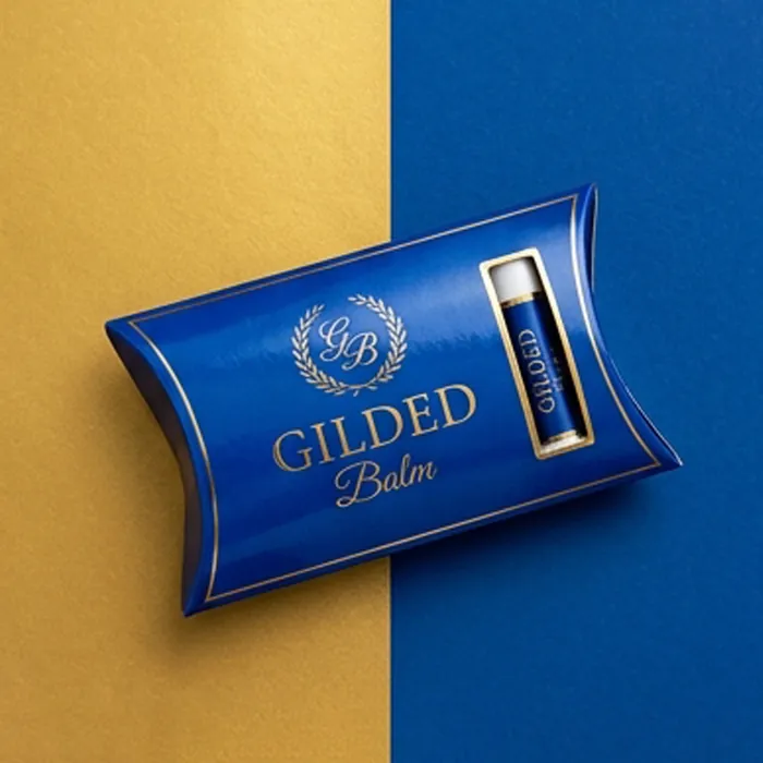 Navy and gold lip balm pillow box with a gilded wordmark and a balm tube