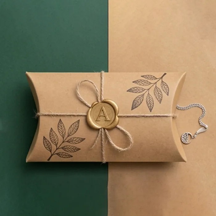 Medium kraft pillow box with a printed botanical seal and a twine tie