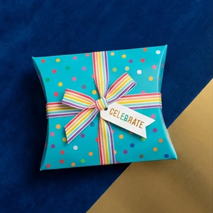 Square pillow box printed with a bright celebratory pattern and ribbon