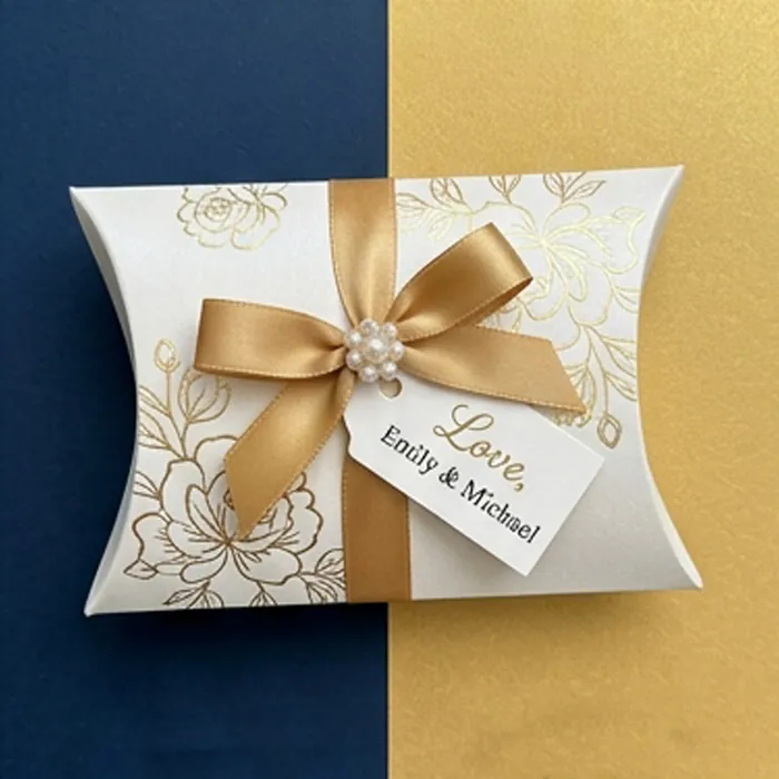 White wedding favor pillow box with a gold ribbon and printed names